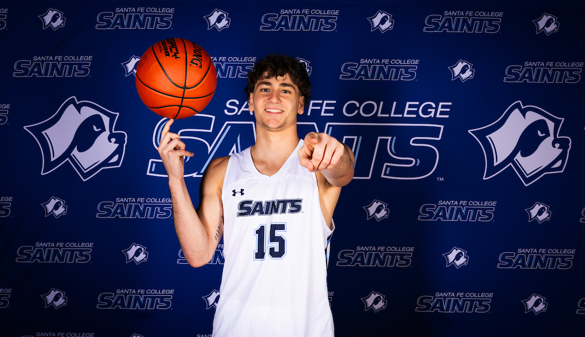 Santa Fe College Saints Men's Basketball player Ryan Webster twirls a basketball on one finger while pointing at the camera.