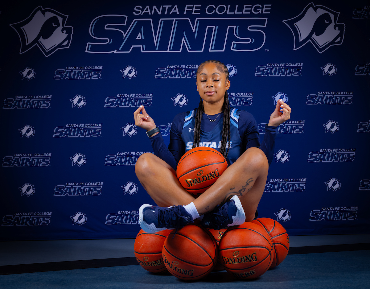 Santa Fe College Saints basketball player Nakayla Green sits atop a stack of basketballs in a meditative pose.