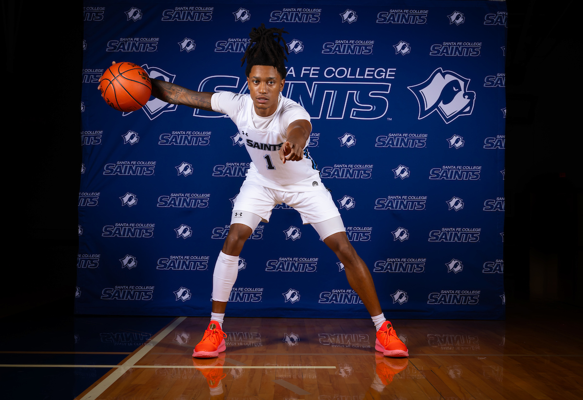 An individual holding a basketball and pointing at the camera.