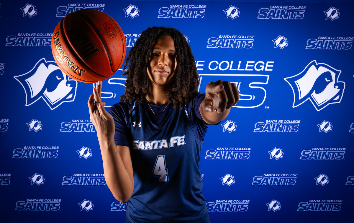 Santa Fe College Saints Women's Basketball player Riana Callihan spins a basketball on their finger while pointing confidently past the camera.