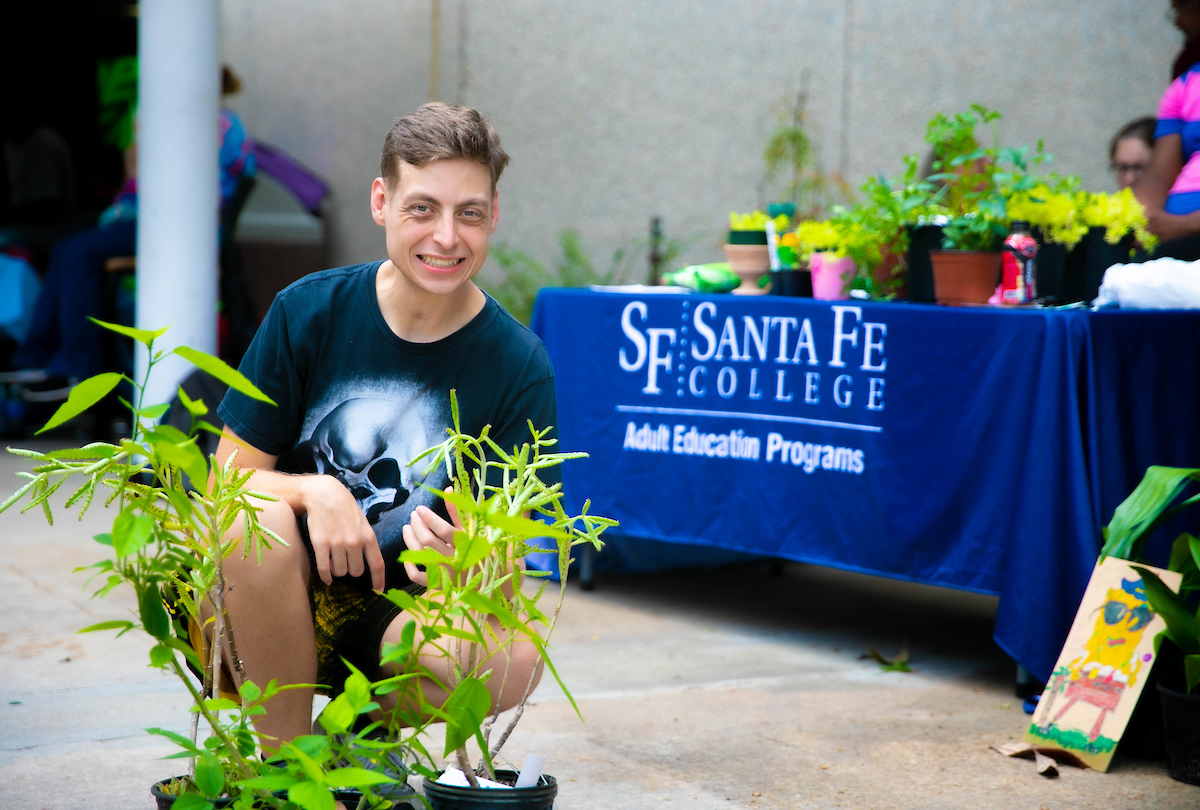 An individual squatting next to plants at a plant sale at Santa Fe College.