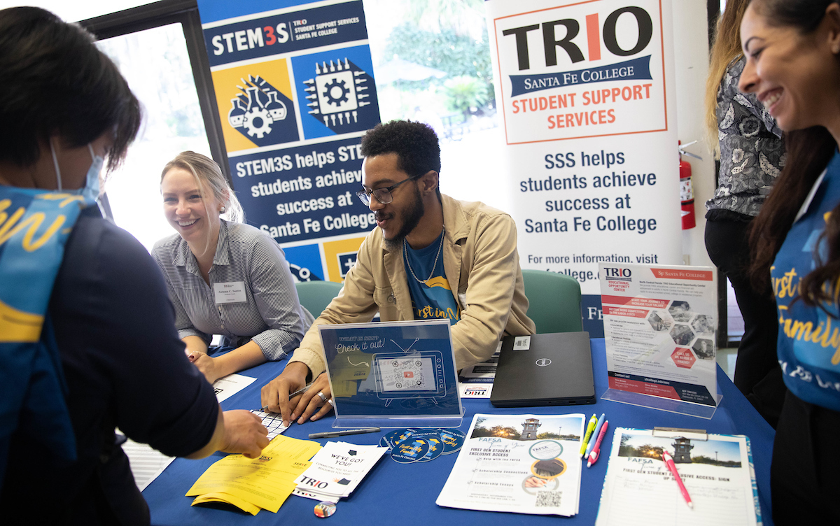 Two individuals assisting a participant at the TRIO table during Santa Fe College's First Gen Day event.