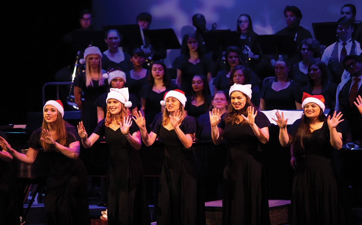 Singers wearing Santa Claus hats perform on stage.