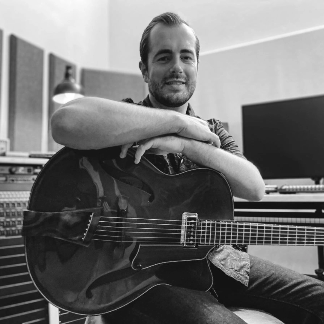 Edward White seated in a studio, holding a guitar.