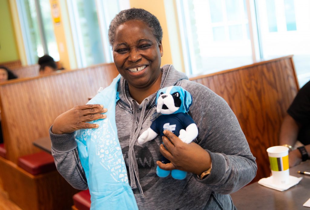 Bea Awoniyi holding a plush Caesar Saint mascot and a Santa Fe College T-shirt