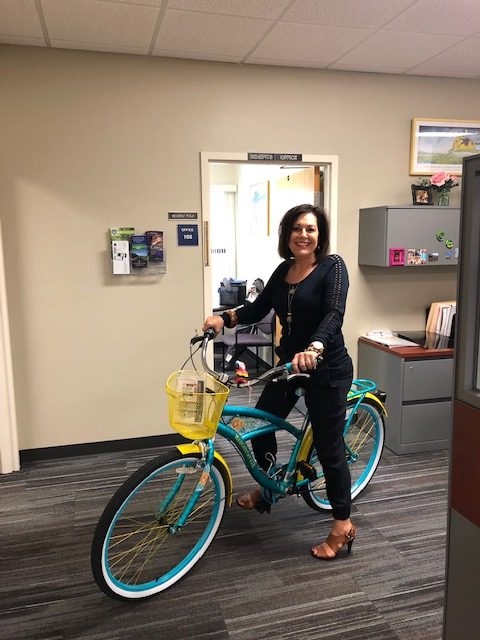 Beverly Polk sitting on a beach cruiser bicycle in the HR office.