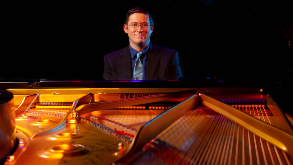 SF Music professor Mitch McKay sitting at an opened Steinway grand piano.