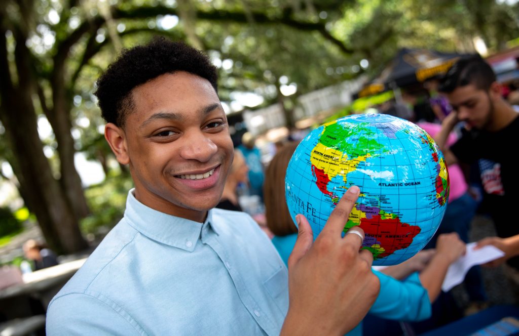 A smiling person points to an inflatable globe while at an outdoor event