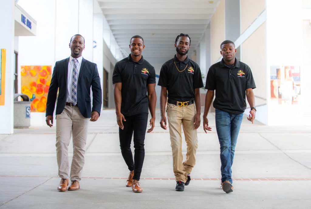 Four individuals dressed in business formal and casual attire walk down an exterior hall toward the camera at Santa Fe College's Northwest Campus