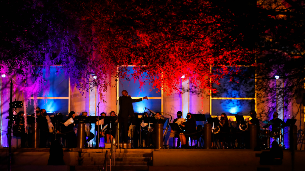 A conductor leads a concert band on stage.