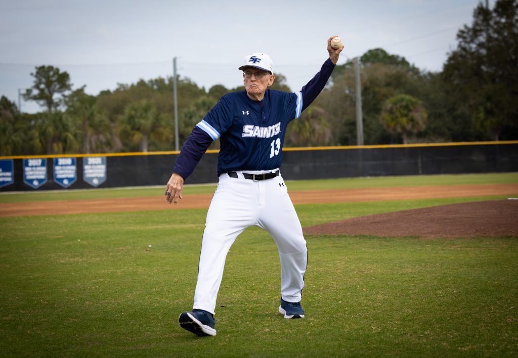 Santa Fe College Saints Baseball coach Harry Tholen throws out the first pitch before a ceremony to rename the field in his honor.