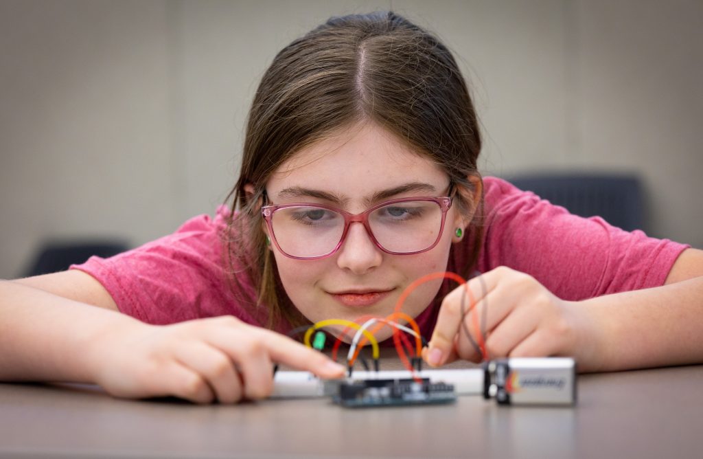 An individual works with a technological device that is connected to a battery.