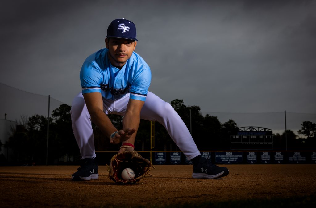 A person in a blue shirt and hat holding a baseball glove on a baseball field.