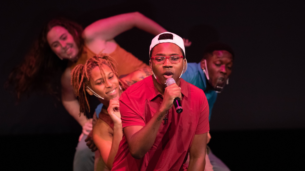 Four individuals sing and perform on stage.