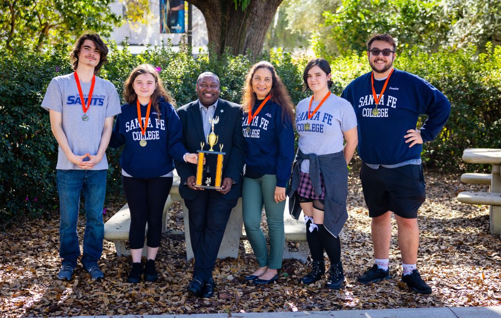 Santa Fe College President Paul Broadie II, Ph.D. with members of the SF Brain Bowl team posing outside with a trophy.