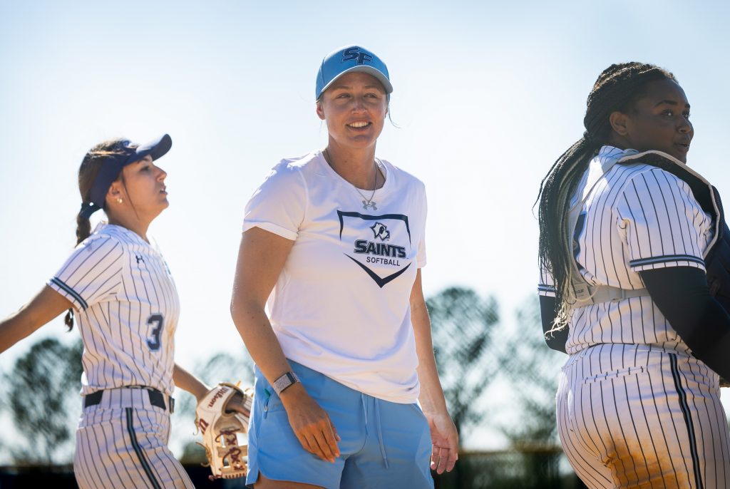 Santa Fe College Saints Softball head coach Savanah Webster standing between two softball players.