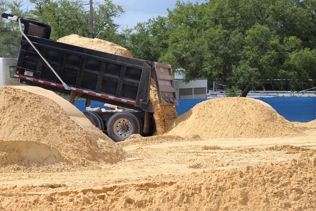 A dump truck dumps sand at a worksite.