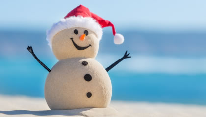 Snowman made of sand with santa hat on beach